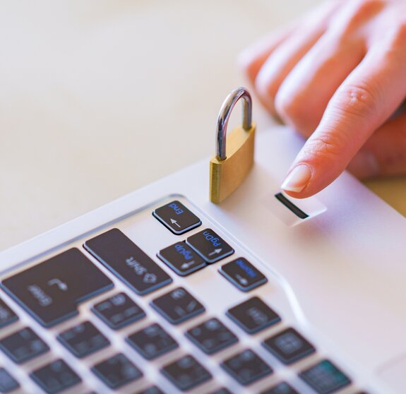 Detailaufnahme eines Fingers, dessen Fingerabdruck zur Identifizierung am Laptop genutzt wird. Daben sieht man ein Sicherheitsschloss.