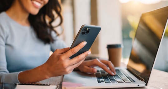 Woman using smartphone and working at laptop computer.