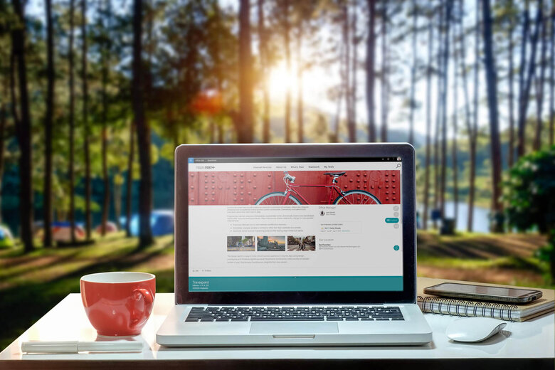 Laptop mit Valo Intranet Seite und mit roter Tasse vor einem Wald.