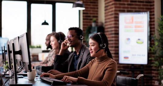 Paralyzed asian receptionist working at call center helpdesk in disability friendly office. Female operator wheelchair user with impairment giving assistance on customer service helpline