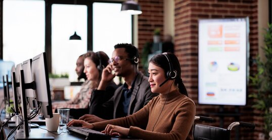 Paralyzed asian receptionist working at call center helpdesk in disability friendly office. Female operator wheelchair user with impairment giving assistance on customer service helpline