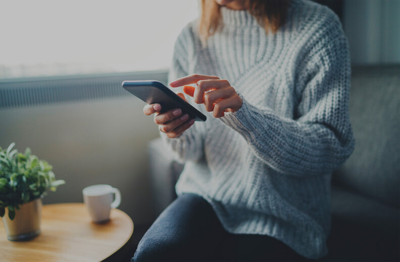 Closeup image of young hipster girl wearing knitted sweater using modern smaertphone device while chilling at home, communication and socail network concept, woman browsing the internet