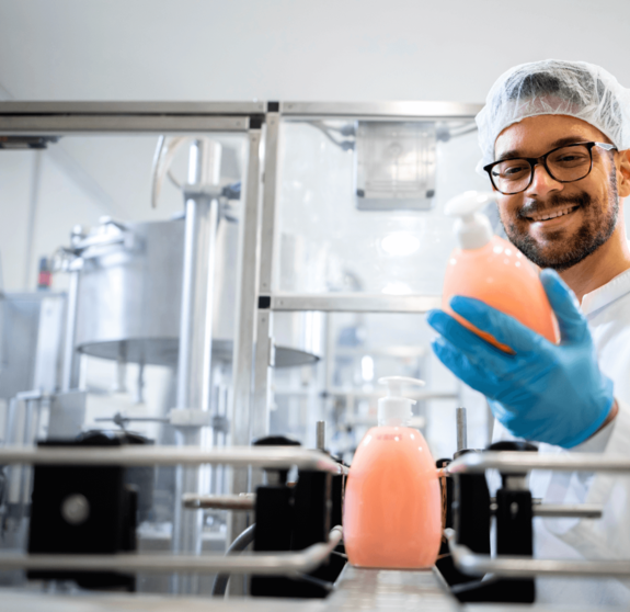 Production line worker or technologist in white sterile uniform working in chemical industry and checking quality of liquid soap or detergent in factory.