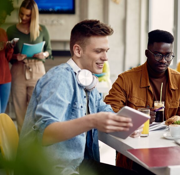 University students using laptop while going through lecture during lunch break in cafeteria.