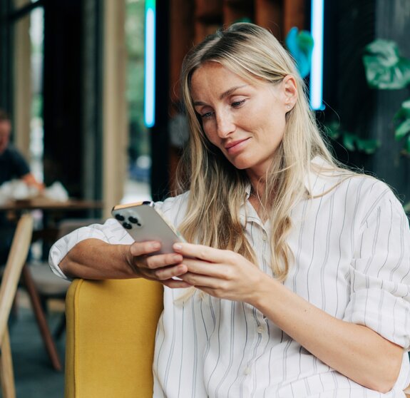 A woman uses a mobile phone to communicate while sitting in a coffee house.