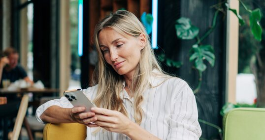 A woman uses a mobile phone to communicate while sitting in a coffee house.