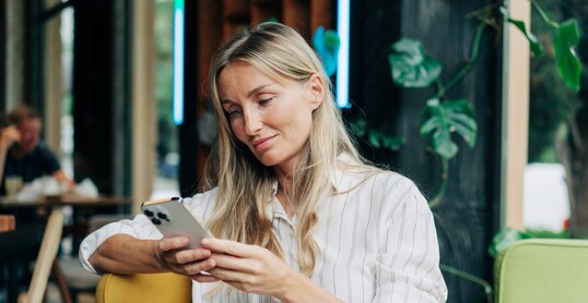 A woman uses a mobile phone to communicate while sitting in a coffee house.