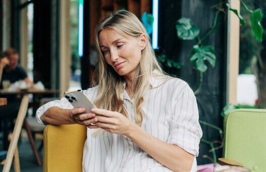 A woman uses a mobile phone to communicate while sitting in a coffee house.