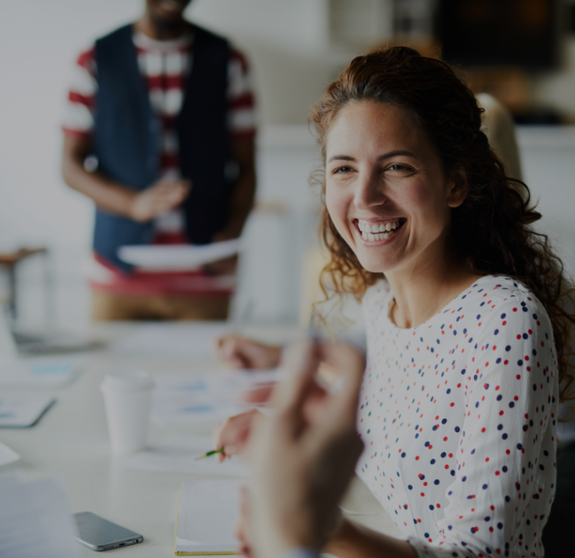 Happy young businesswoman sitting at desk and communicating with her colleagues during a meeting