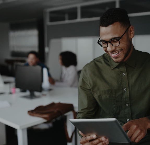 Cheerful young businessman using digital tablet smiling while his colleagues working at the background