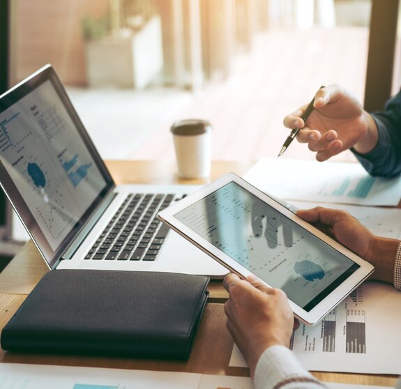 Business partnership coworkers using a tablet to chart company financial statements report and profits work progress and planning in office room.