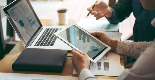 Business partnership coworkers using a tablet to chart company financial statements report and profits work progress and planning in office room.