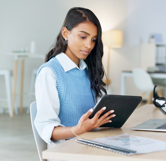 Trendy marketing professional using an online app to network, meet deadlines and stay connected during office hours. Young business woman using her laptop and tablet while working in the office