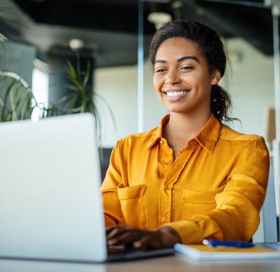 Happy black businesswoman using laptop typing and working online while sitting at workplace in office, copy space