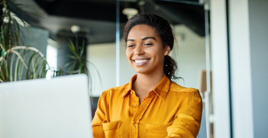 Happy black businesswoman using laptop typing and working online while sitting at workplace in office, copy space