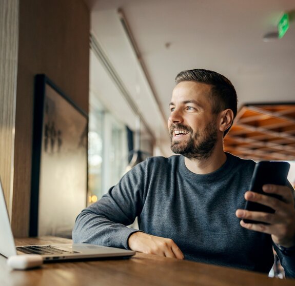 A happy casual entrepreneur is sitting in coffee shop and working on e-commerce by using cutting edge technologies.