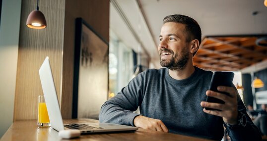 A happy casual entrepreneur is sitting in coffee shop and working on e-commerce by using cutting edge technologies.