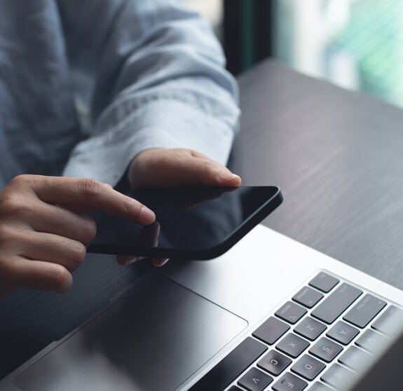 Closeup of woman finger touching on mobile phone screen. Asian woman using smartphone while sitting at table with laptop computer at home office, online shopping, mobile banking, internet payment