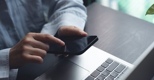 Closeup of woman finger touching on mobile phone screen. Asian woman using smartphone while sitting at table with laptop computer at home office, online shopping, mobile banking, internet payment