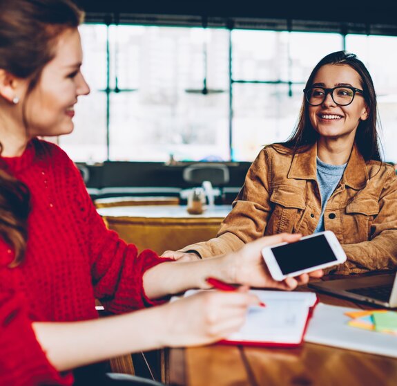 Two happy female friends enjoying positive conversation looking to each other in break of learning and searching information for test indoors, smiling hipster girls talking and spending time together