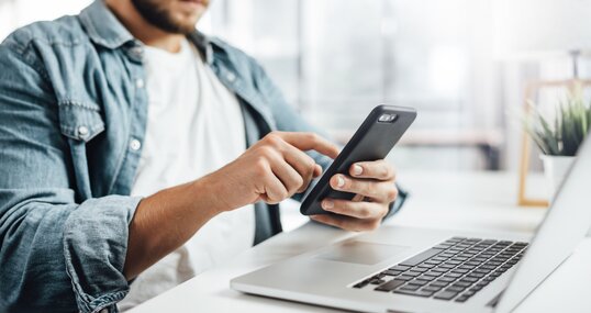 Young man with smartphone in his hands. Modern businessman at sunny office. Freelancer at work.