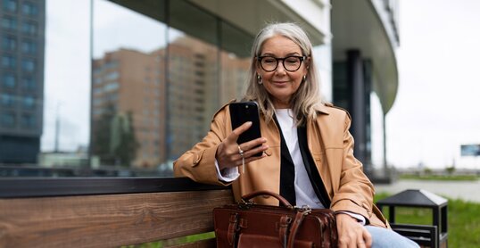 an older woman with a mobile phone sits on a bench outside