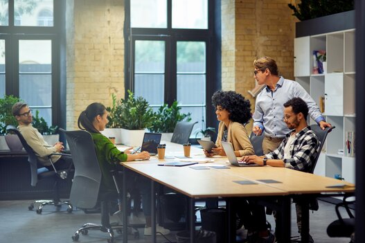 Office life. Group of young multiracial people sitting at the table in coworking space and working together, using modern technologies and discussing project