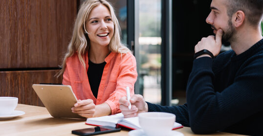 Cheerful caucasian female student looking a her male friend discussing learning project on cafe break, prosperous young man and woman employees talking to each other about business ideas on meeting